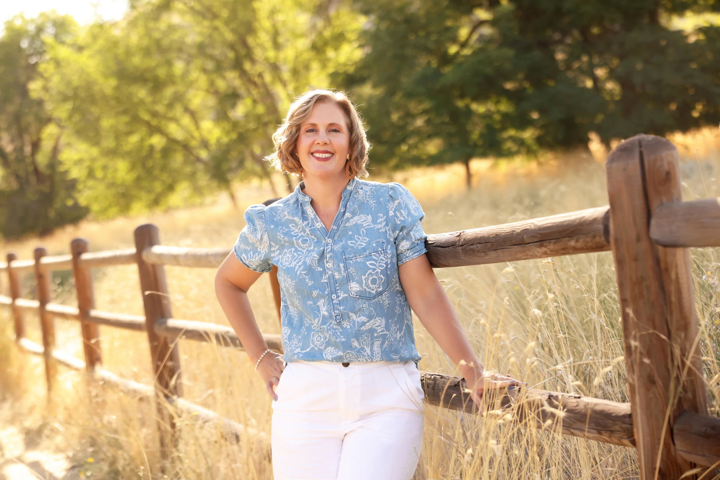 Cacey Klein smiling beside a wooden fence in a sunlit Idaho field.